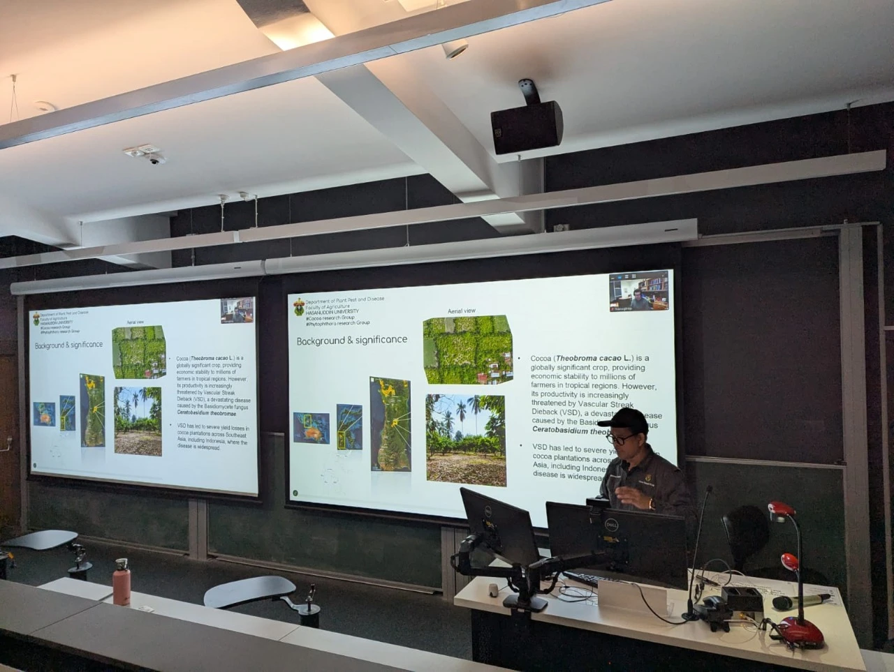 Dr. Muhammad Junaid, S.P., M.P., Ph.D., is delivering his seminar presentation as part of the Phytophthora and Cocoa Research Groups, affiliated with the Faculty of Agriculture. He is shown in a lecture theatre (LT 327) at the Carslaw Building, presenting the seminar series for SoLES F&A on May 9, 2025. Credit: Jun.